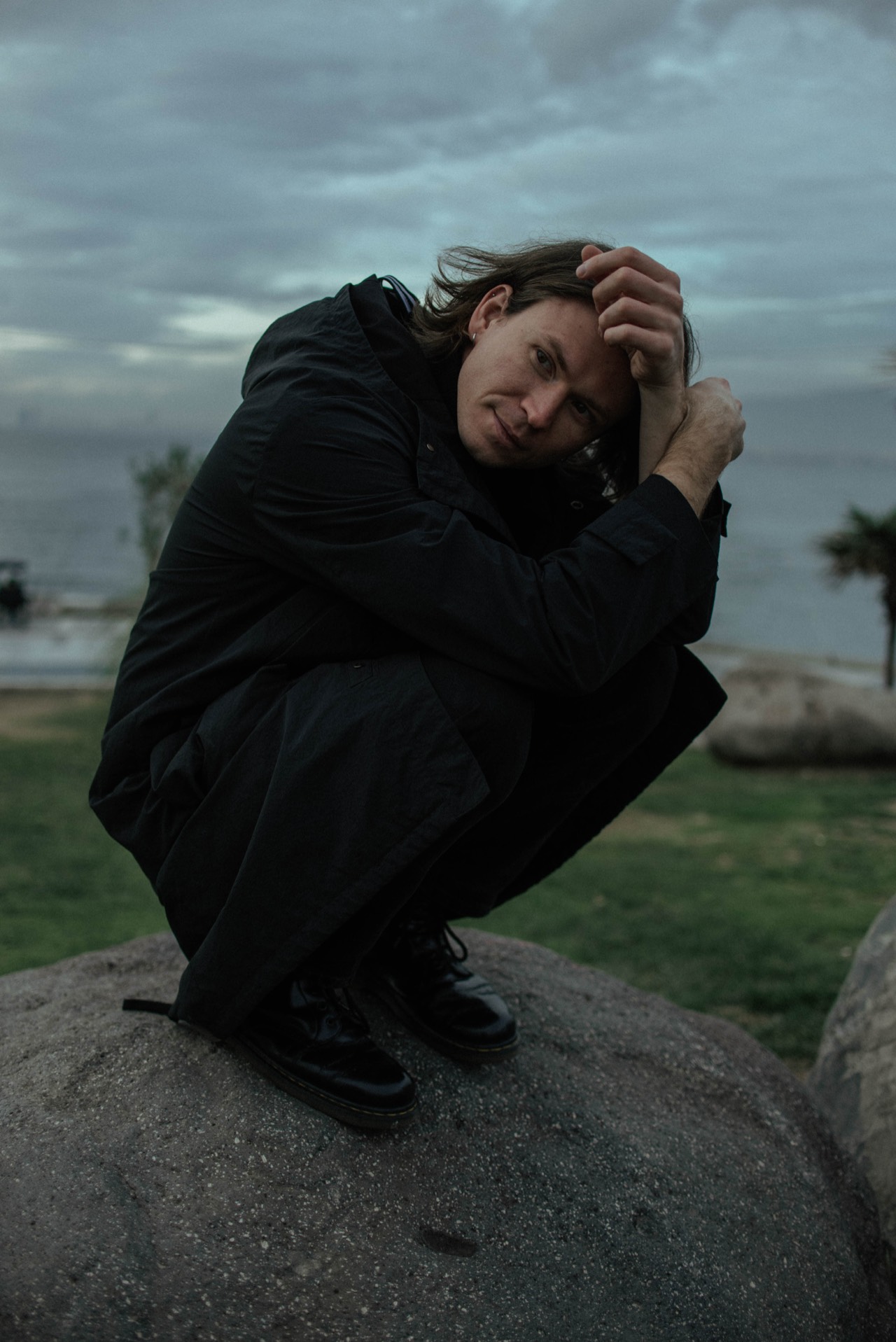 Crouched on a boulder by the sea at dusk